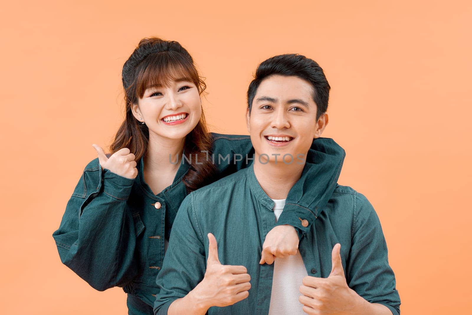 Happy young couple showing thumbs up and looking at camera isolated over yellow background by makidotvn