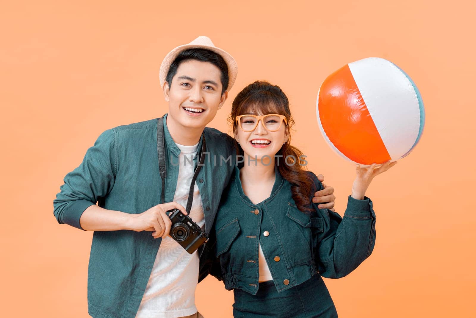 Young attractive couple with beach ball and camera on yellow background