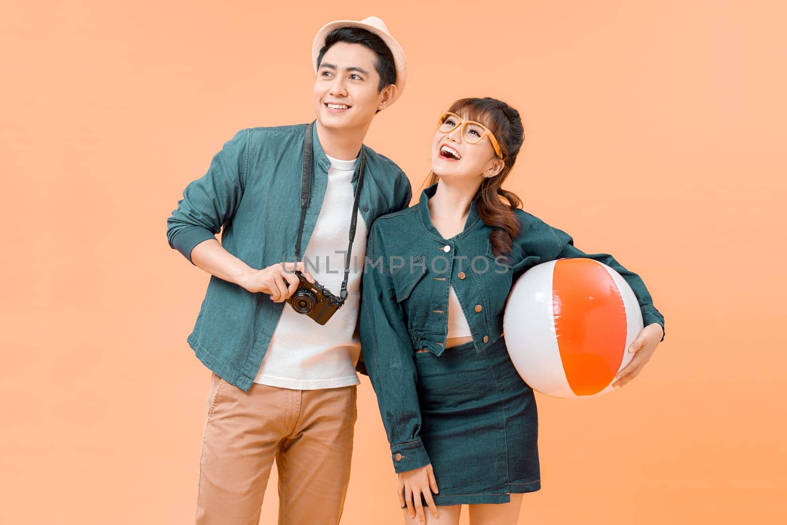 Young attractive couple with inflatable ball and camera on yellow background