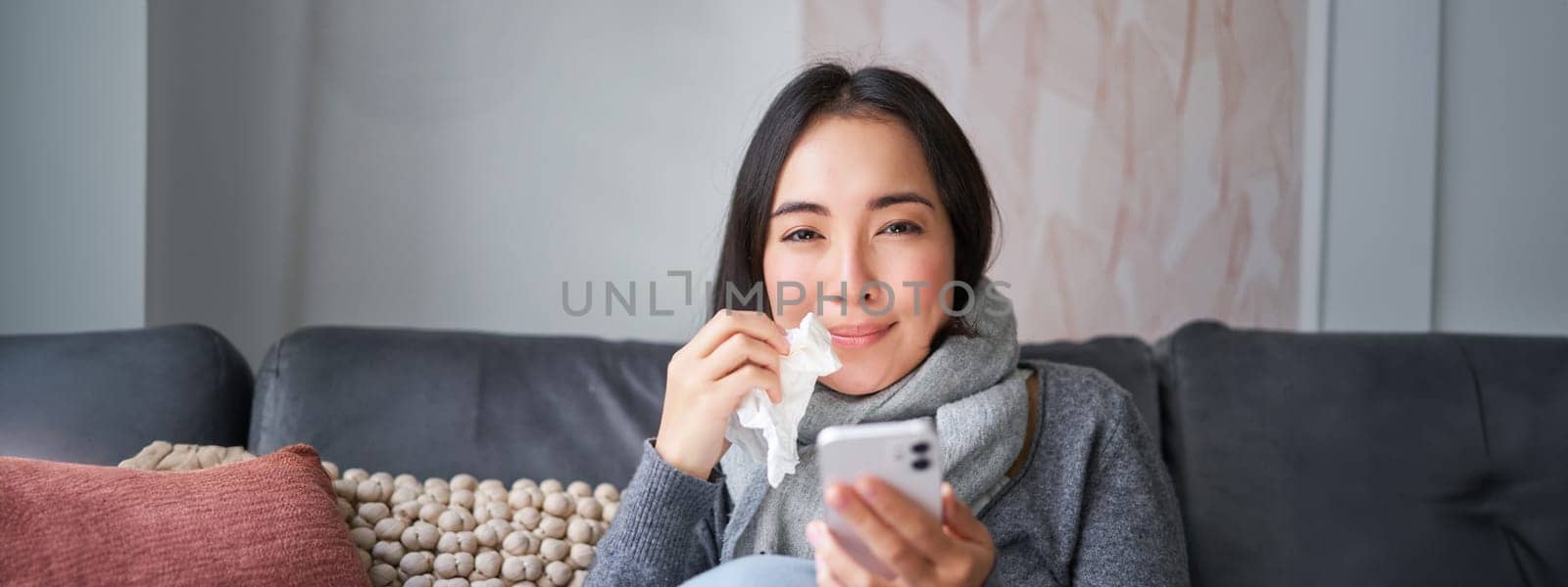 Portrait of sick woman contacting her GP via mobile phone while catching cold, sitting with flu at home, using smartphone by Benzoix