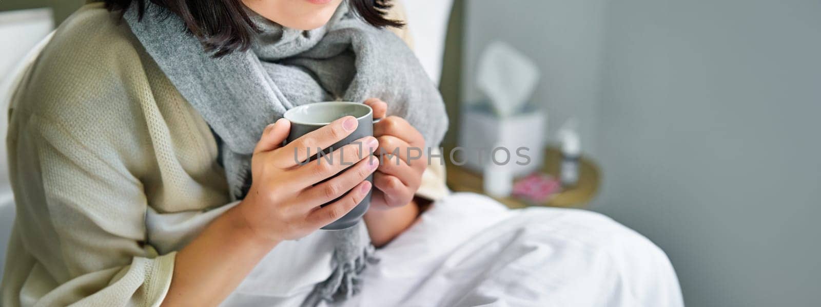 Close up of female hands holding hot drink, lying in bed, girl catching a cold and staying at home.