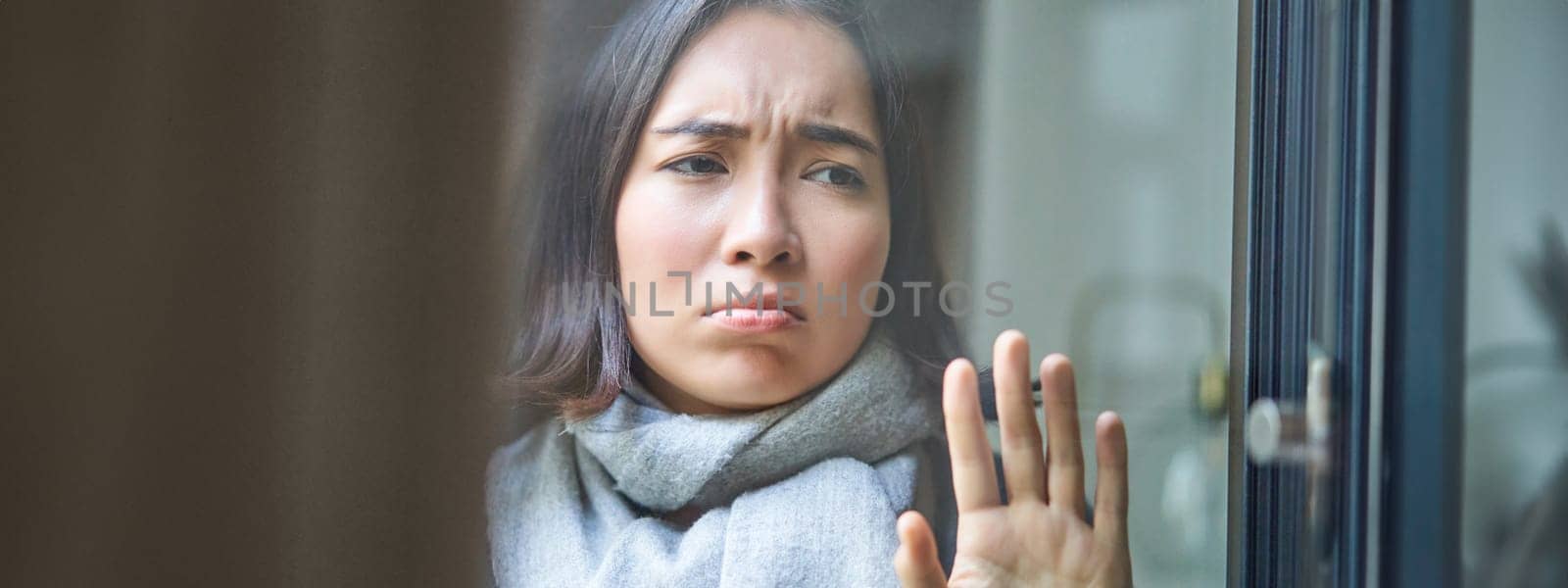 Portrait of sad ill woman staying at home, looking out of the window with jealous and upset face, cant leave home as being sick with covid-19 by Benzoix