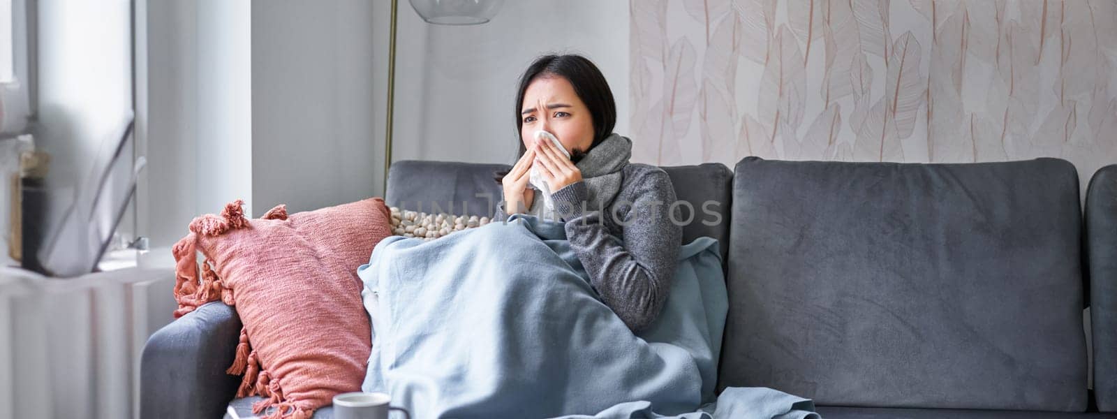 Korean woman feels unwell, sneezing and coughing, catching cold, staying at home with fever and temperature, taking medication.