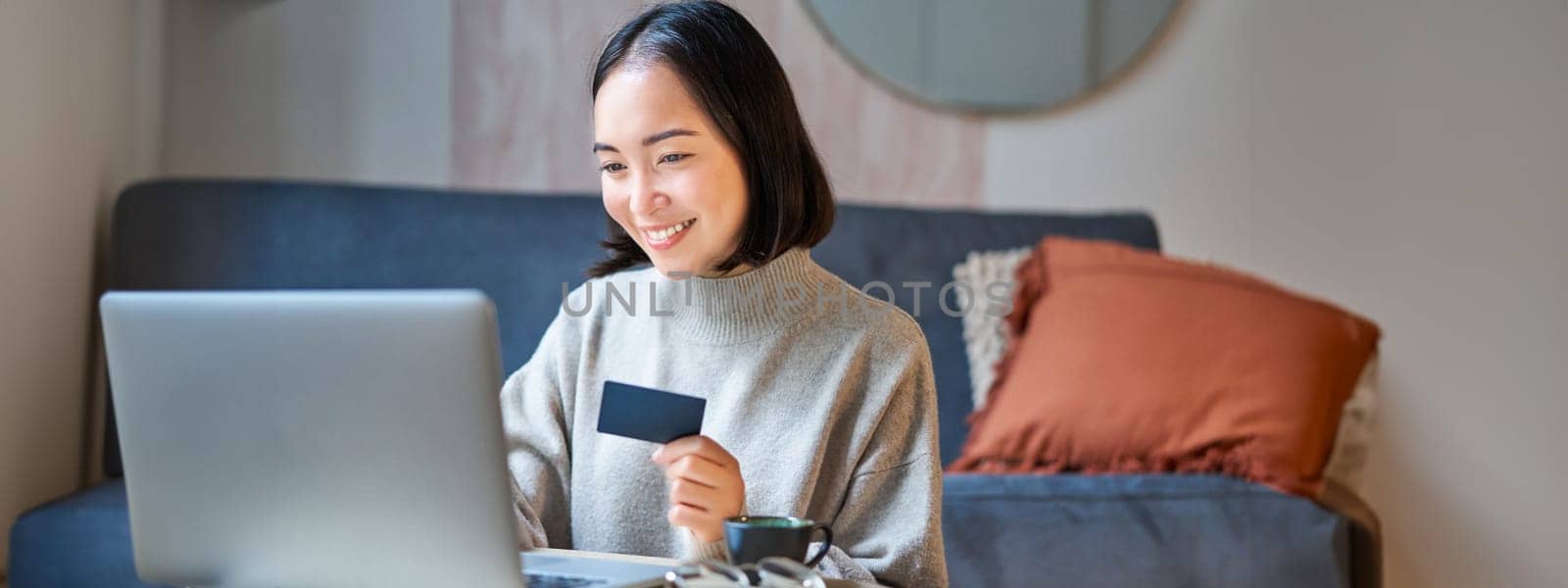 Portrait of korean woman shopping online, using her credit card and laptop to order delivery from website.