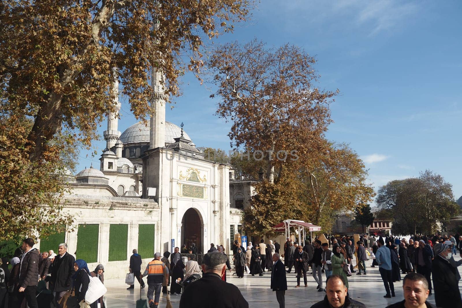 A lively crowd gathers at a historic mosque, surrounded by colorful autumn foliage