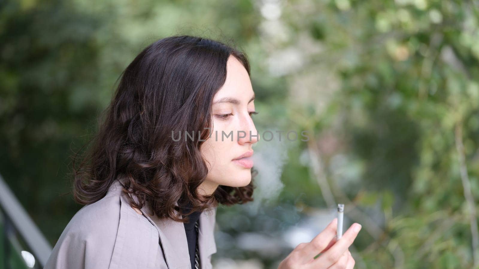 A young woman with beautiful curly hair is thoughtfully smoking a cigarette while enjoying a serene outdoor setting