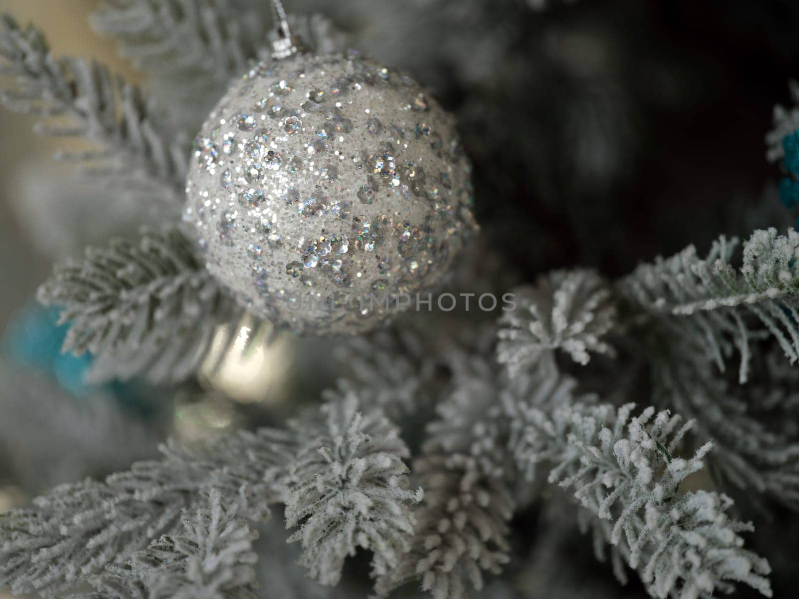 An exquisite silver ornament, beautifully adorned with glitter, hangs delicately on a frosted Christmas tree