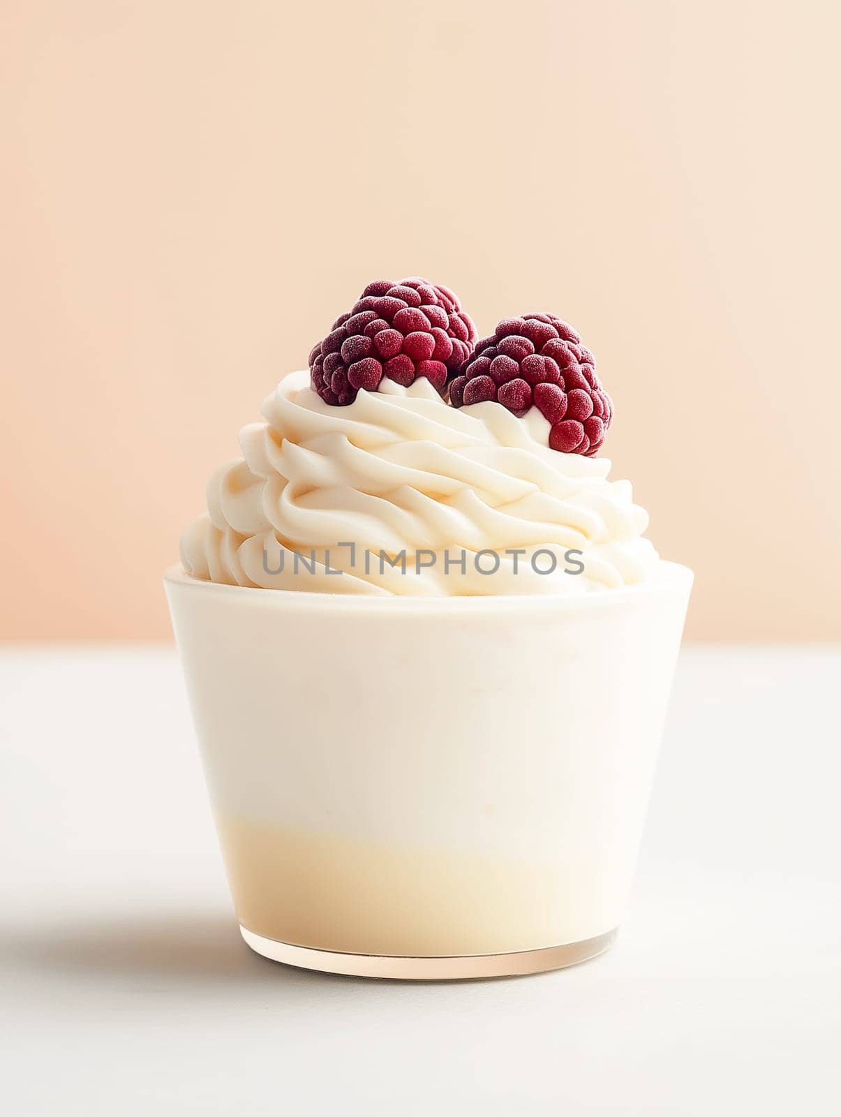 A cupcake with whipped cream and raspberries on top. The whipped cream is fluffy and the raspberries are frozen. The cupcake is sitting on a white table