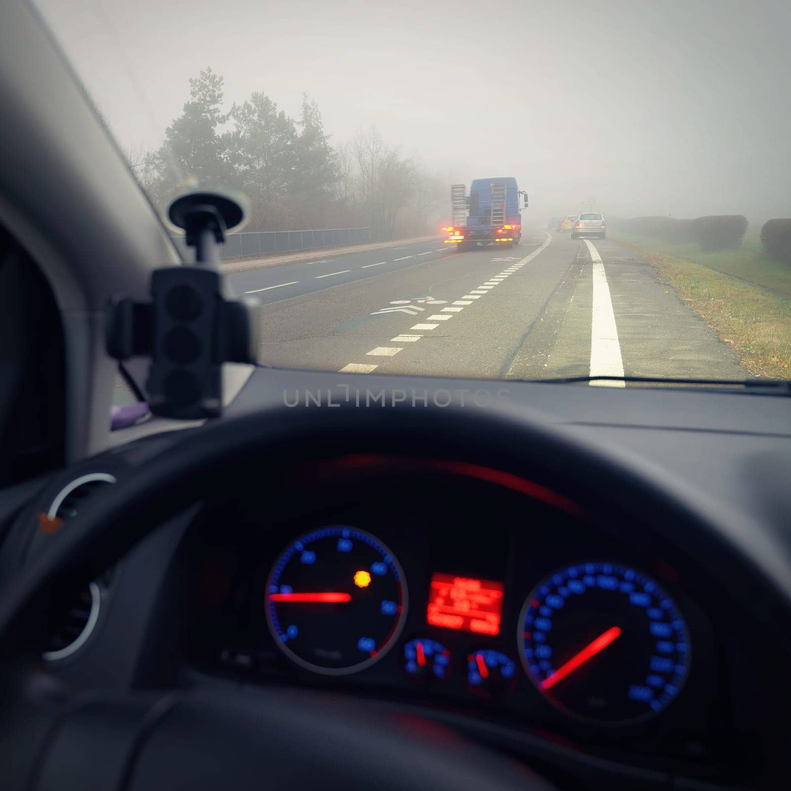 Car traveling on the foggy road with headlights or headlamps on. Low visibility - Dangerous driving of cars in winter in bad weather