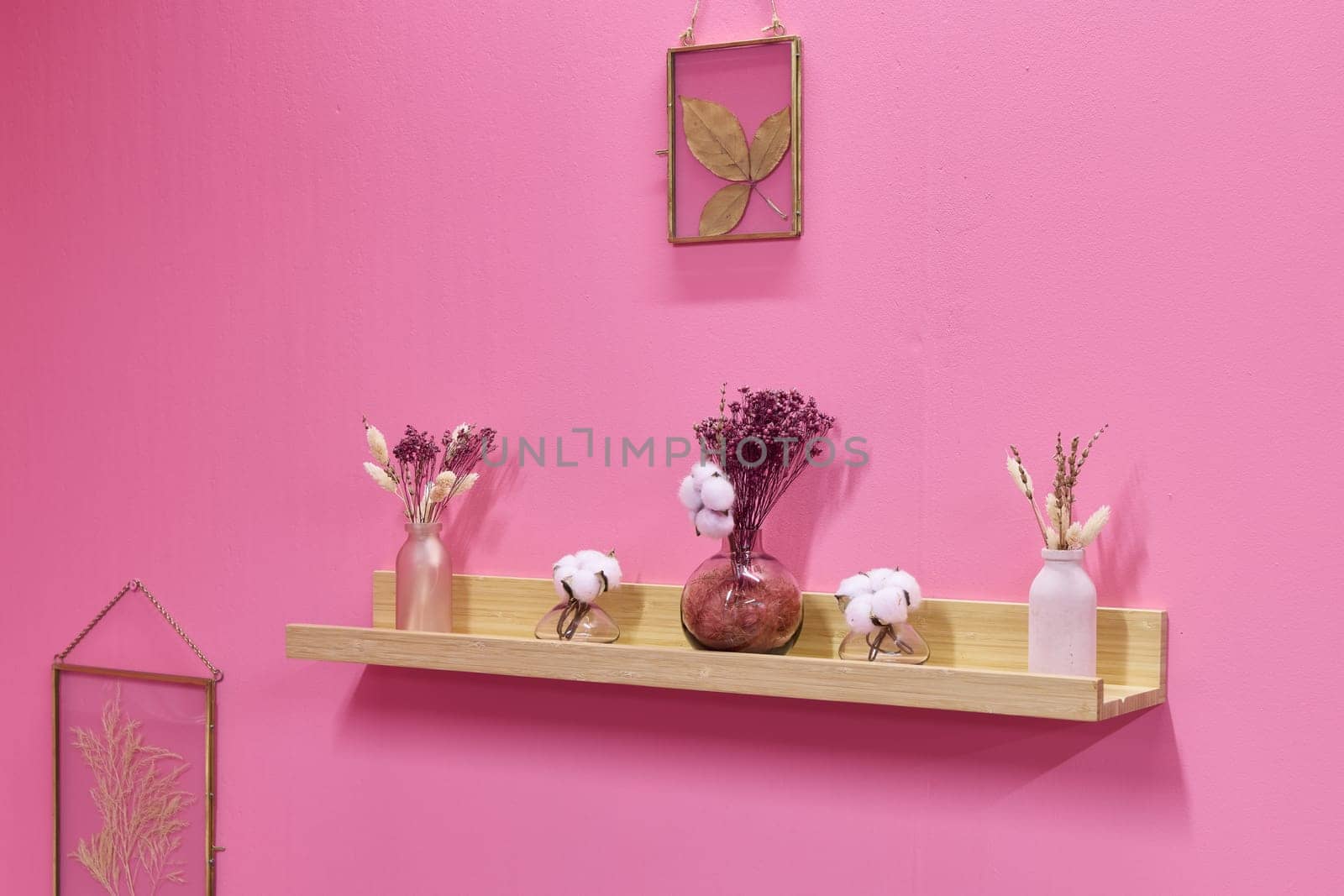 A colorful display of dried flowers on a rustic shelf, set against a soft pink background for added charm