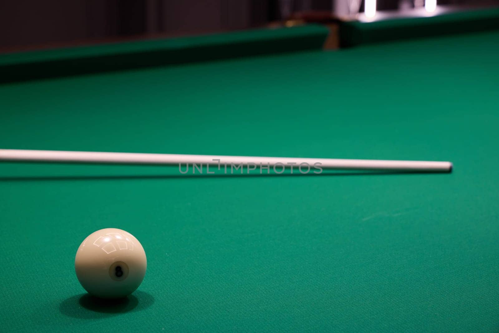 Closeup of a pristine white ball, elegant cue stick, and vibrant green felt pool table, capturing billiards