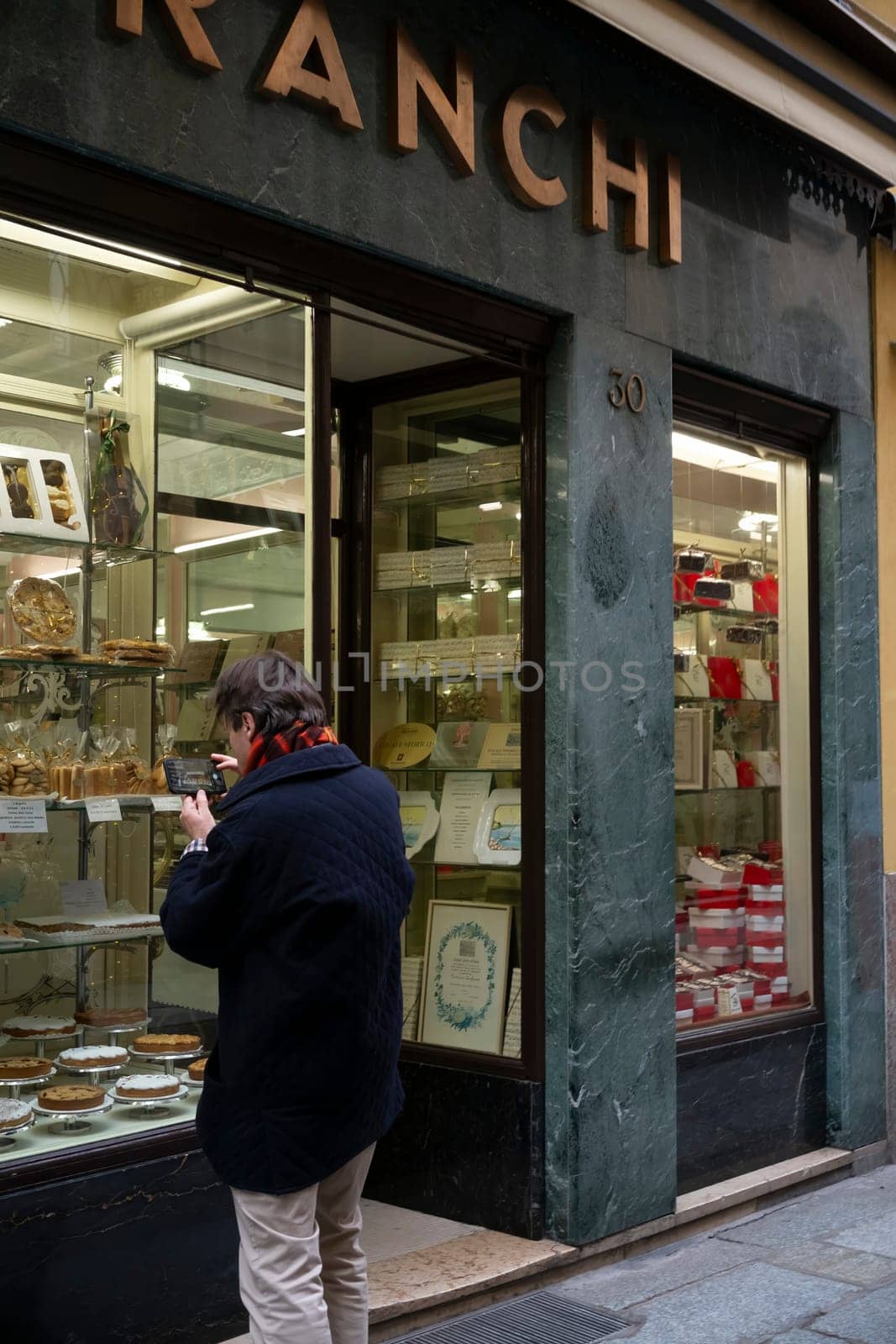 Cremona, Italy - November 20th 2024 Tourist taking pictures of a traditional pastry shop window displaying various desserts and awards in cremona, italy