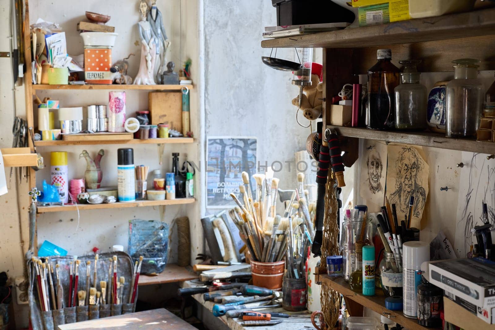 A cluttered artist's studio showcases various tools, paint brushes, and colorful supplies scattered across shelves. Sunlight floods the space, highlighting the creative chaos within.