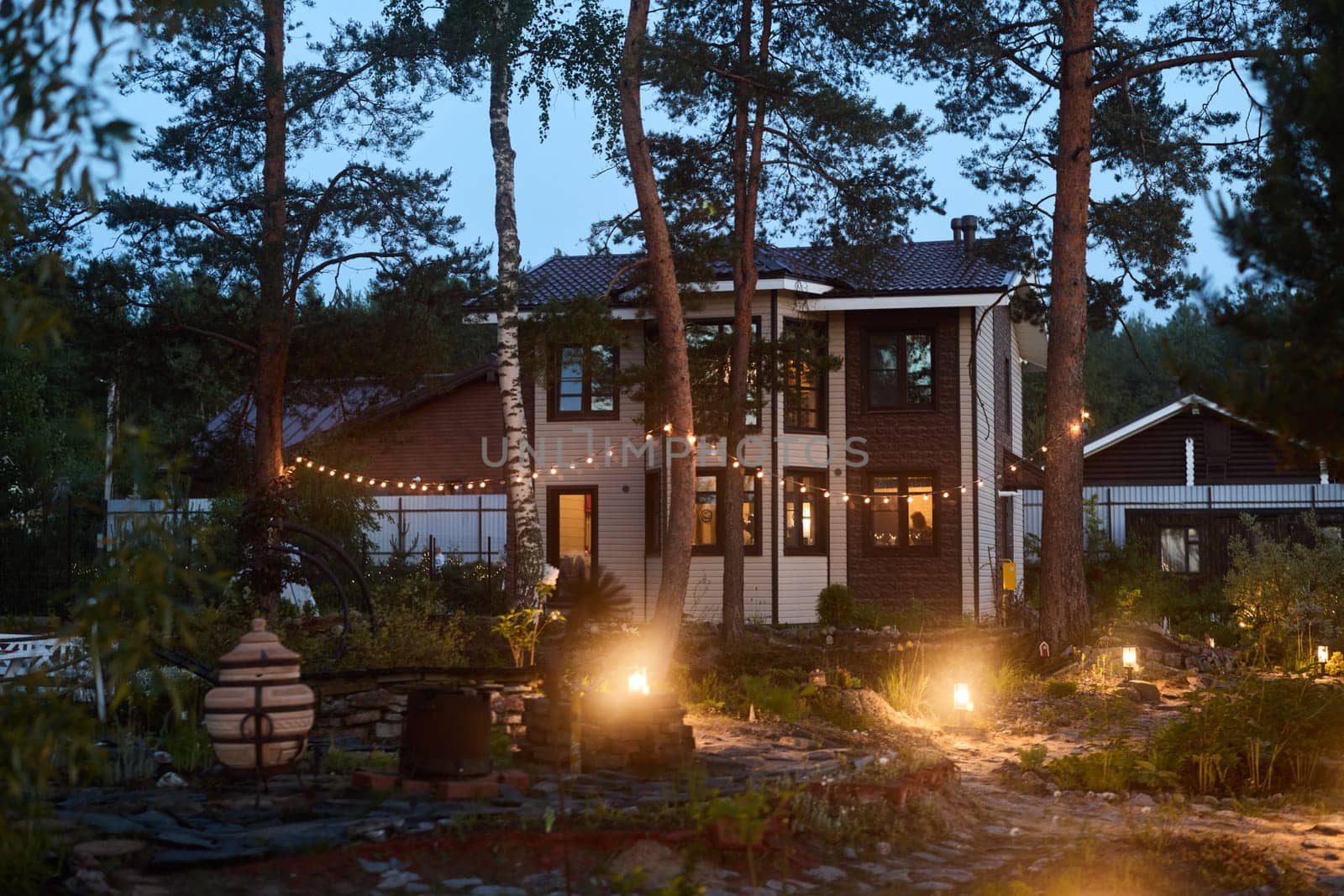 A tranquil house peacefully admiring the stunning glow of dusk, embraced by trees and surrounded by warm garden lights