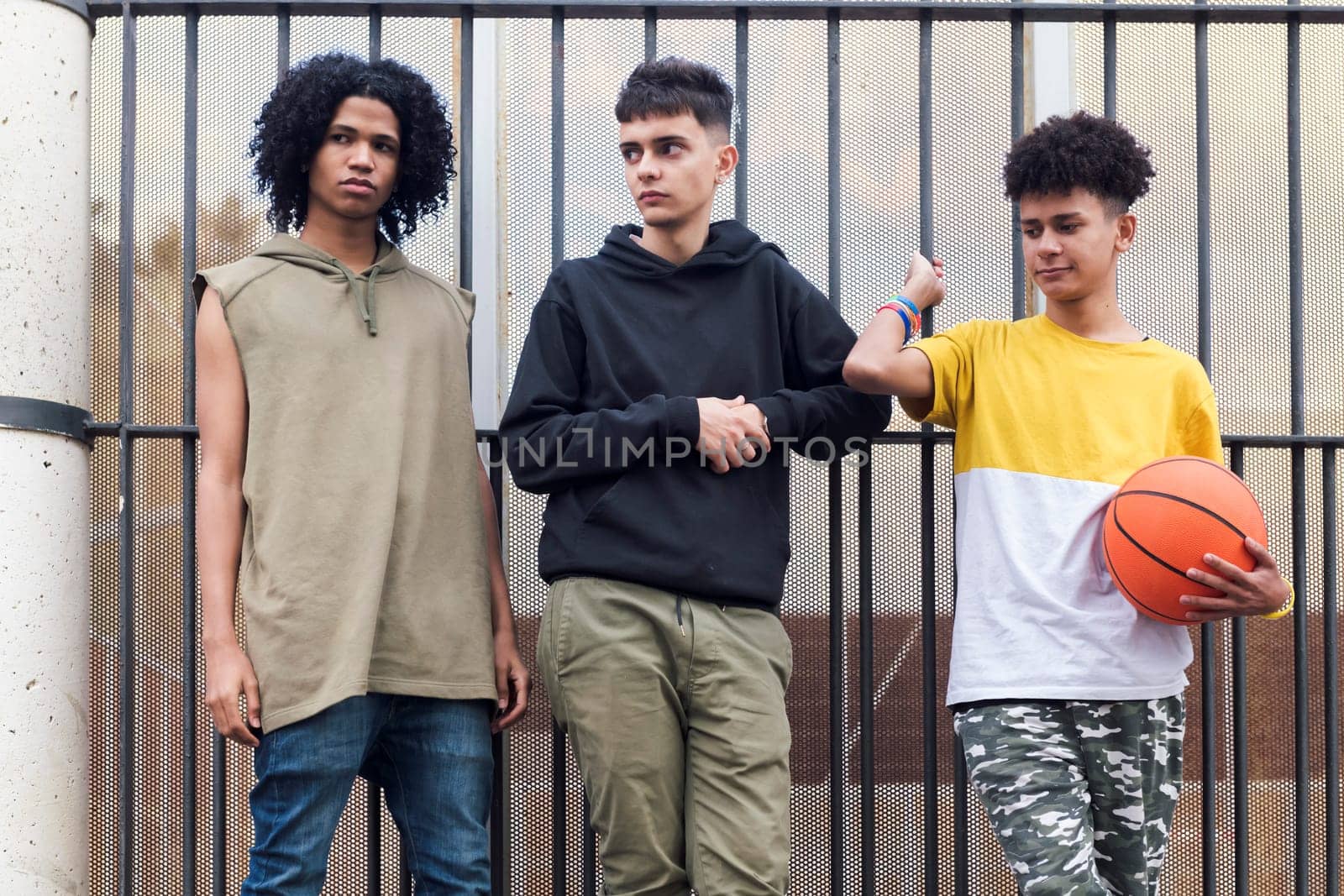 three serious multiracial male teenagers with basketball standing together on street, concept of friendship and urban lifestyle