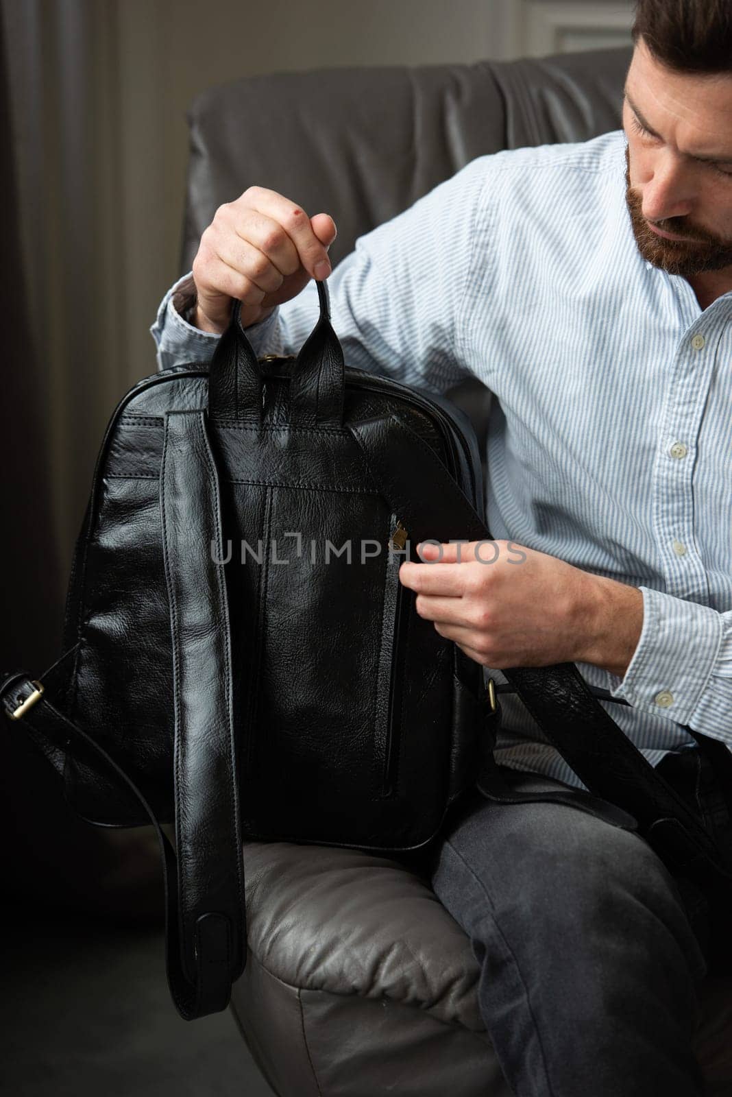 A man is comfortably seated in a chair with a backpack resting beside him, creating a relaxed and casual atmosphere around him