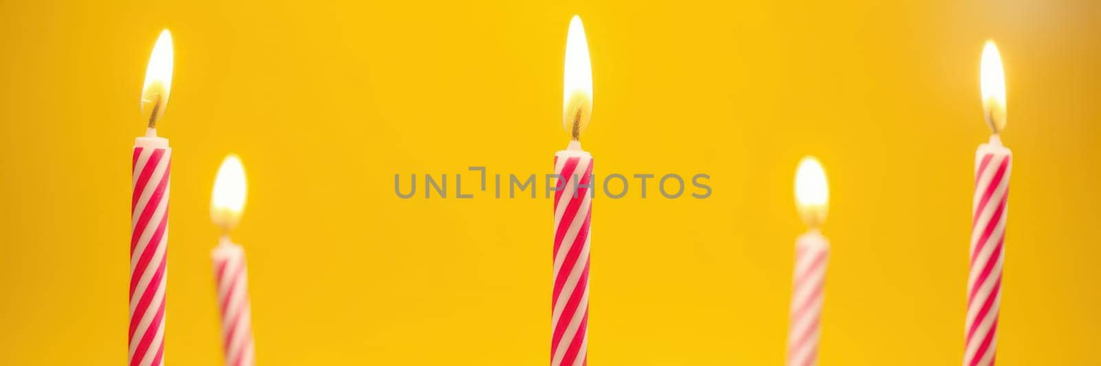 Colorful candles with pink stripes and flames stand upright against a bright yellow backdrop, creating a festive atmosphere perfect for celebrations.