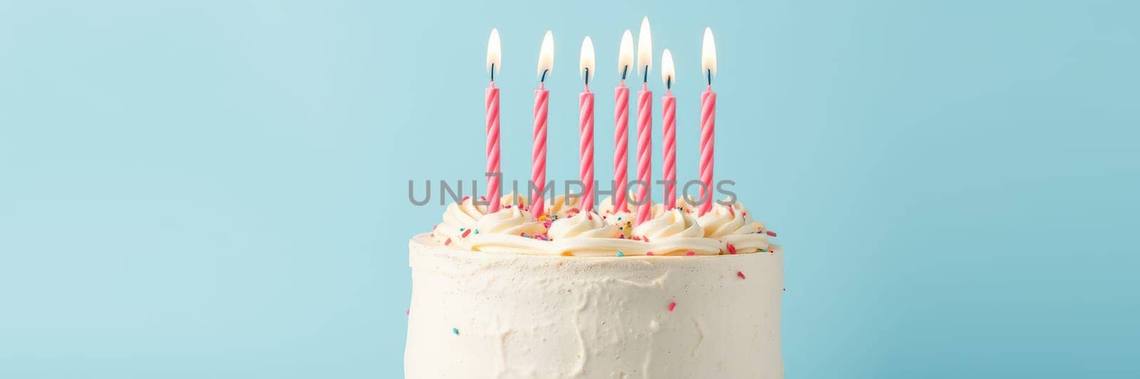 A white frosted birthday cake sits on display featuring pink striped candles, colorful sprinkles, and a vibrant blue backdrop, perfect for a festive celebration.