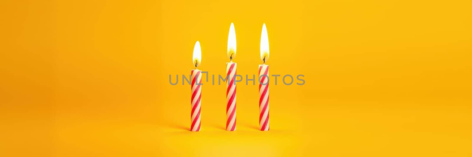 Three striped candles burn brightly against a vivid yellow backdrop, adding a cheerful touch perfect for birthday festivities or joyful gatherings.