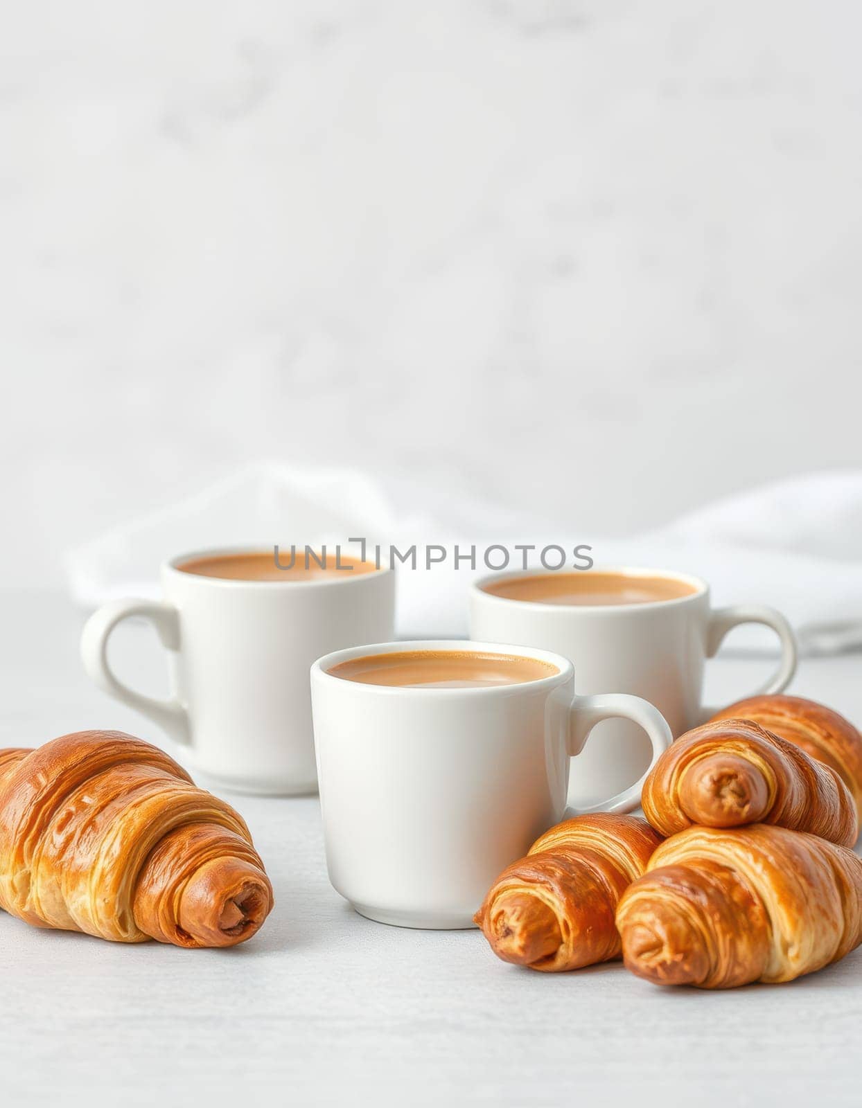Three white cups filled with rich coffee are arranged beside delicious, flaky croissants on a light-colored table. The scene is bright and inviting, perfect for a morning indulgence.