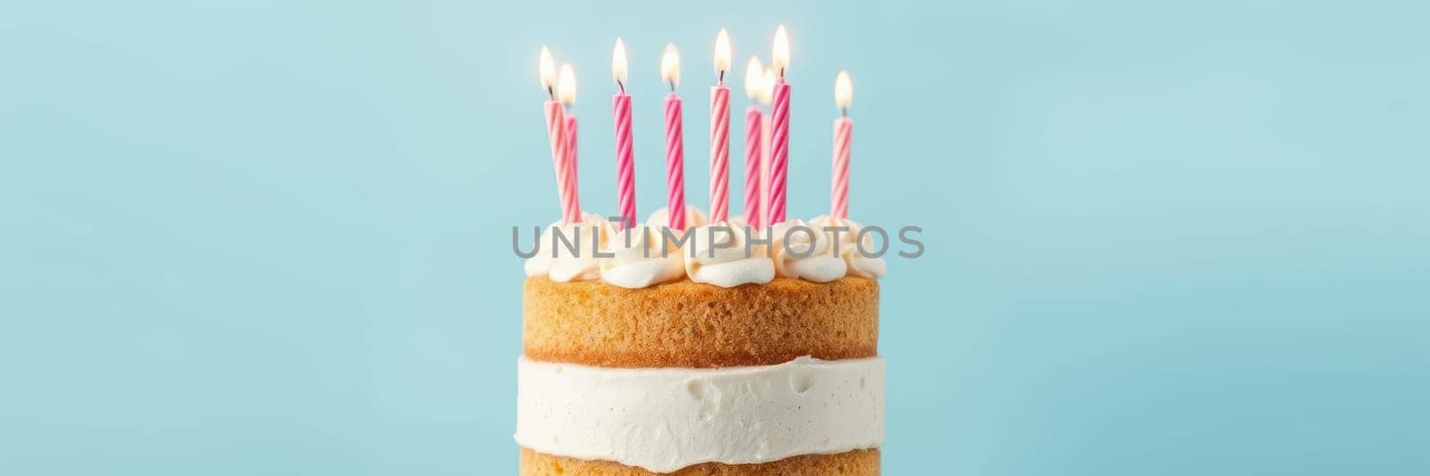 A tall, round cake with icing and a layer of cream sits against a blue backdrop. Multiple candles are lit on top, ready for celebration at a birthday party.