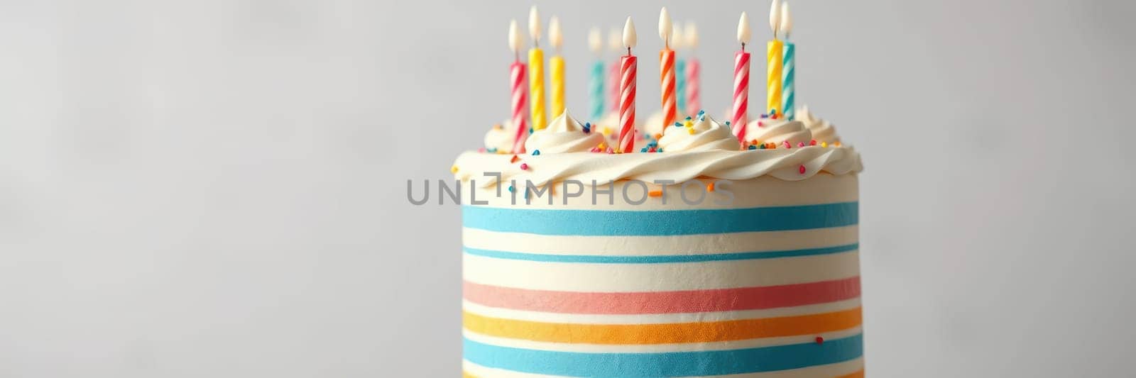 A festive cake featuring bright stripes and topped with lit candles. It serves as a centerpiece for a birthday celebration, conveying joy and anticipation.