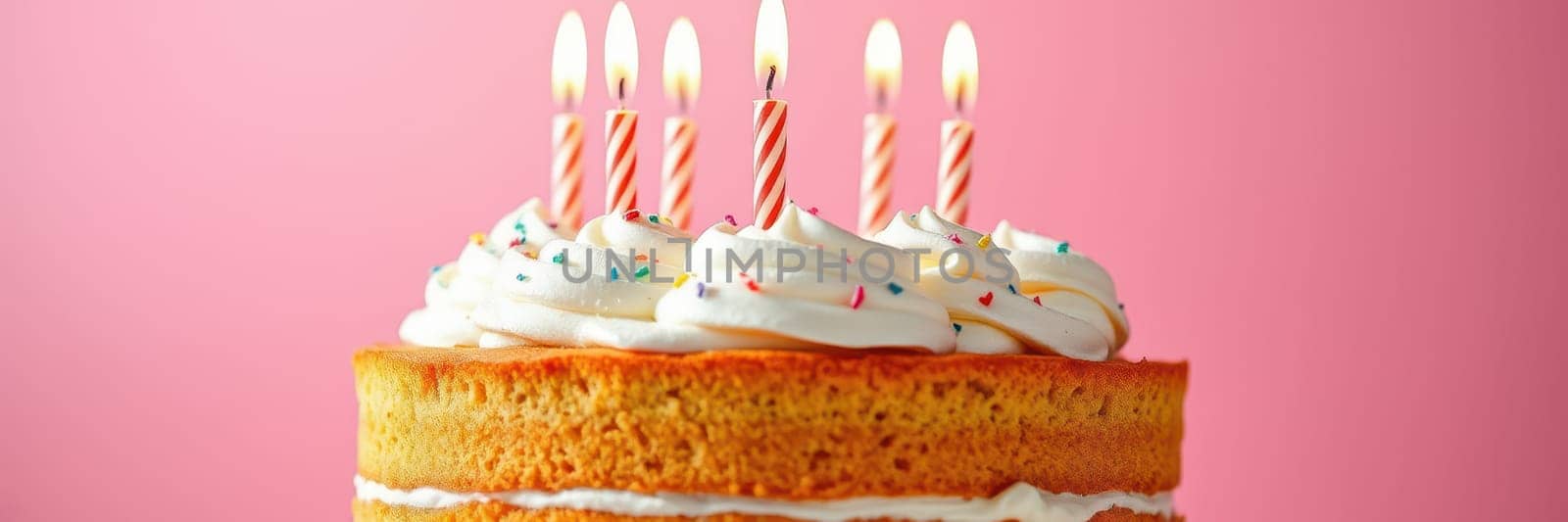 A delectable birthday cake sits in front of a pink background, adorned with swirls of icing and colorful sprinkles, featuring six lit candles ready for celebration.