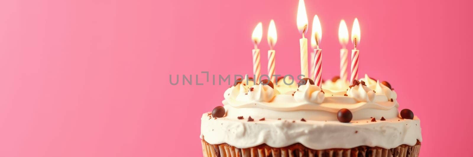 A beautifully decorated birthday cake sits prominently, adorned with colorful icing and lit candles, ready for celebration against a cheerful pink backdrop.