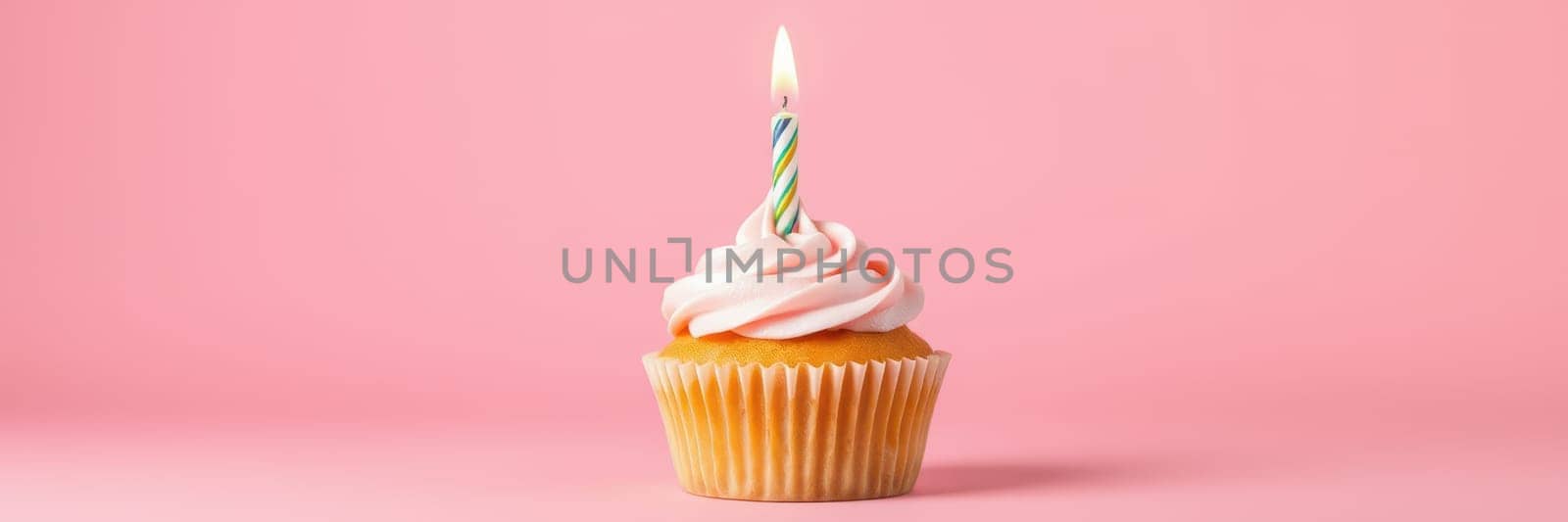 A vibrant cupcake sits on a light pink surface, topped with swirls of soft pink frosting and a colorful candle, perfect for a birthday celebration or sweet occasion.