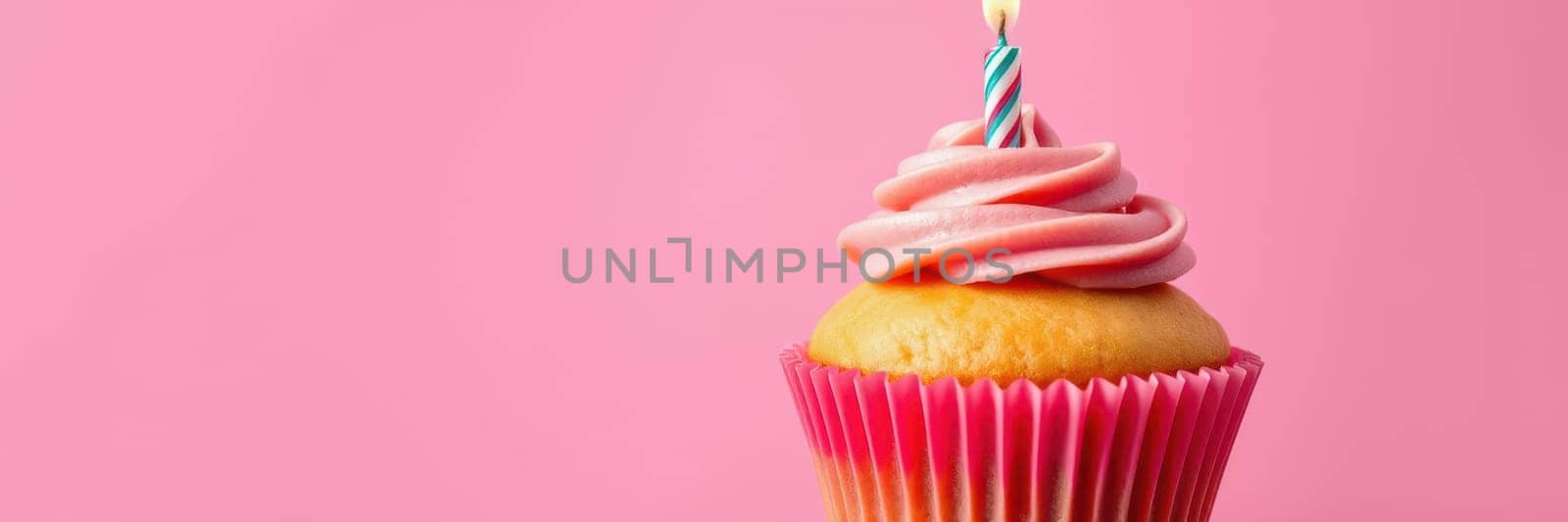 A beautifully decorated cupcake topped with swirls of pink frosting and a lit candle sits prominently against a bright pink background. Perfect for any festive occasion.