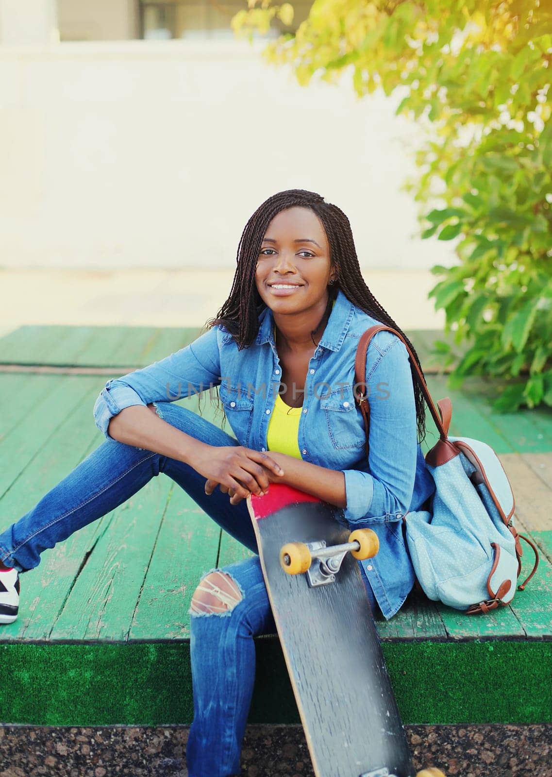 Portrait of happy smiling young african woman model posing with skateboard in the city