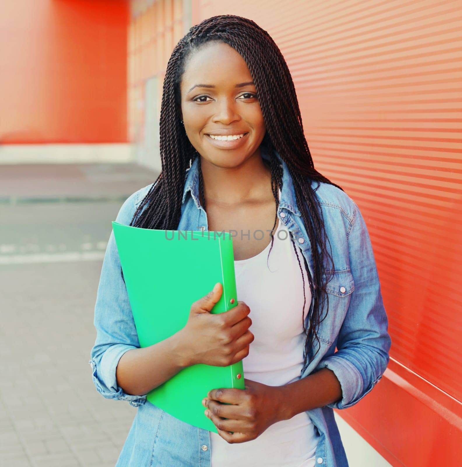 Portrait of happy African young woman student holding folder with documents, smart black smiling girl in casual looking at camera standing in the city