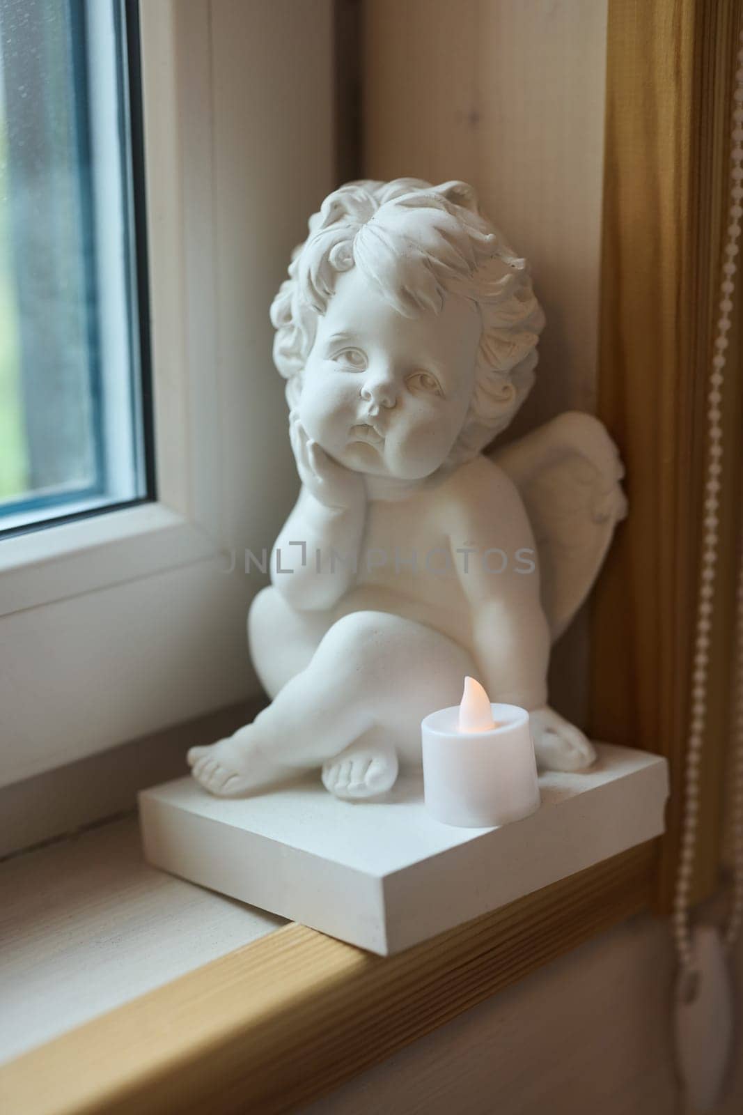 A serene angel statue rests beside a flickering candle on a window ledge, capturing tranquility and calm