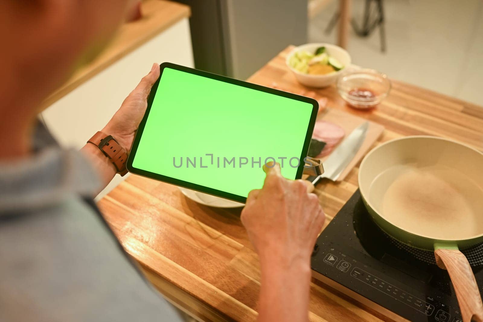Close up of senior man using digital tablet in a cozy home kitchen to follow a recipe or cooking instructions.