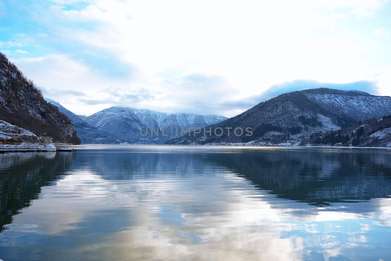 A tranquil fjord in Gaupne, Norway, surrounded by snowy mountains and reflecting calm waters, showcasing serene winter beauty. 