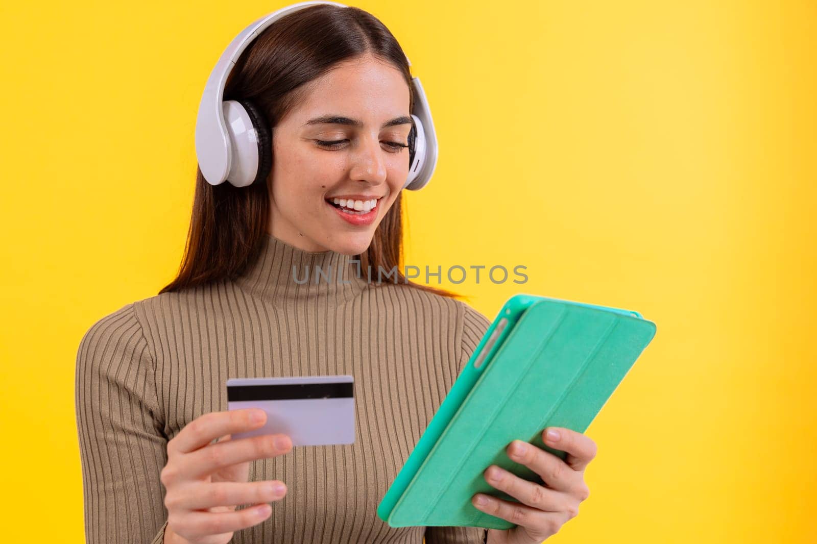 A woman smiles while holding a tablet and a credit card in front of a bright yellow background. His joyful expression creates a positive and engaging atmosphere.