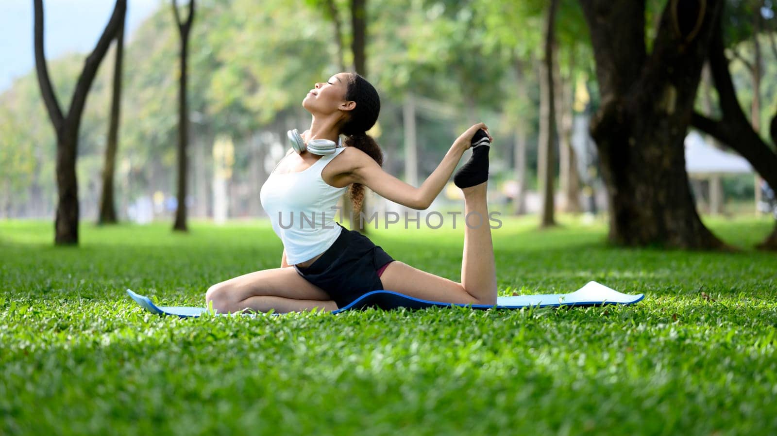 Peaceful young woman practicing yoga on a mat in a sunny park.