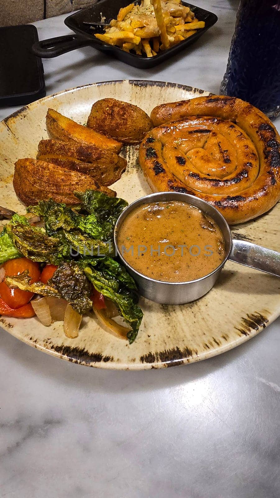 mouthwatering German worst curled up cumberland sausage meal featuring a grilled sausage, loaded cheese fries, and fresh vegetables served on a rustic plate. Perfect for dinner lovers appreciating hearty and flavorful dishes.
