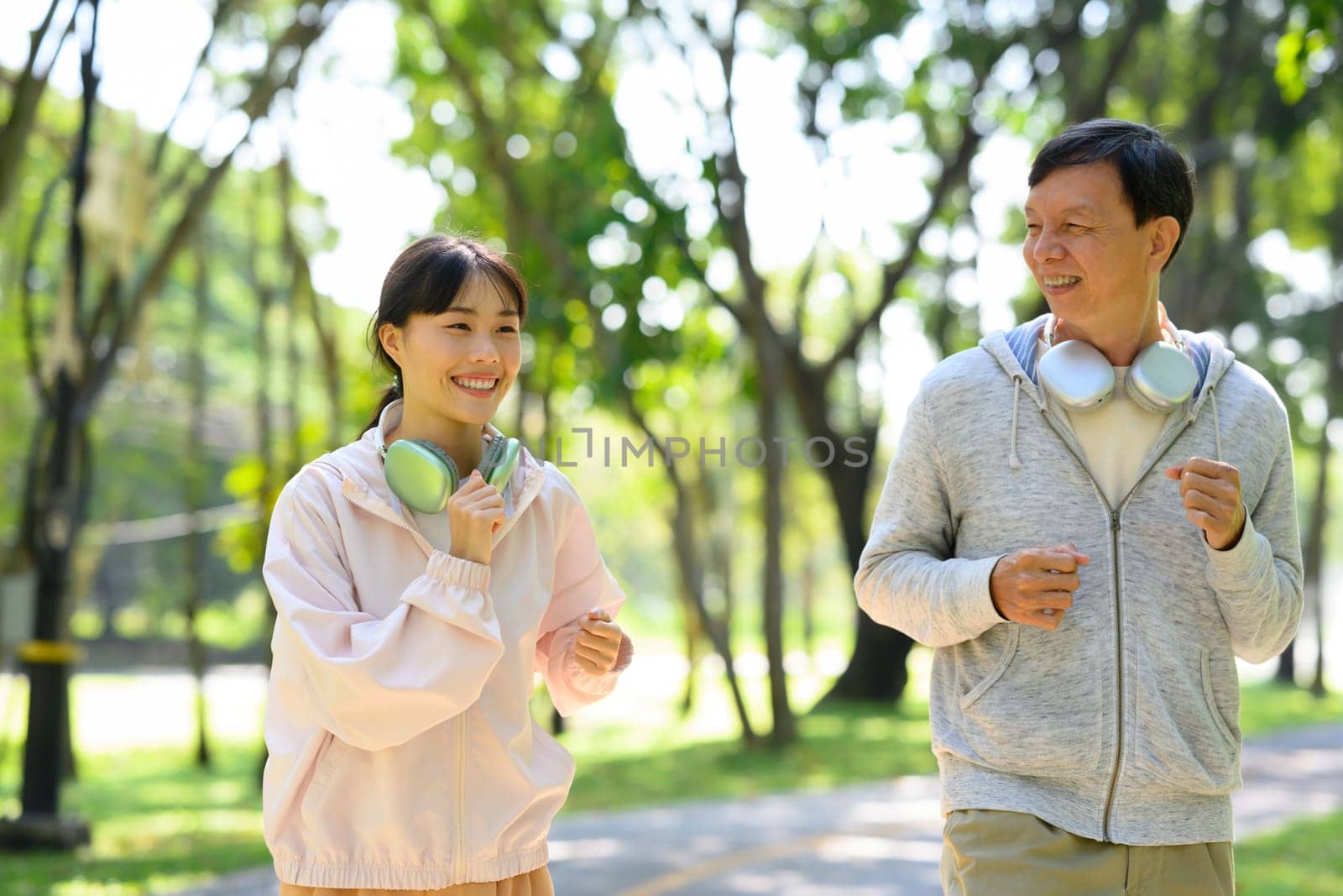 Cheerful father and daughter jogging on a sunny park path. Health and family activity concept.