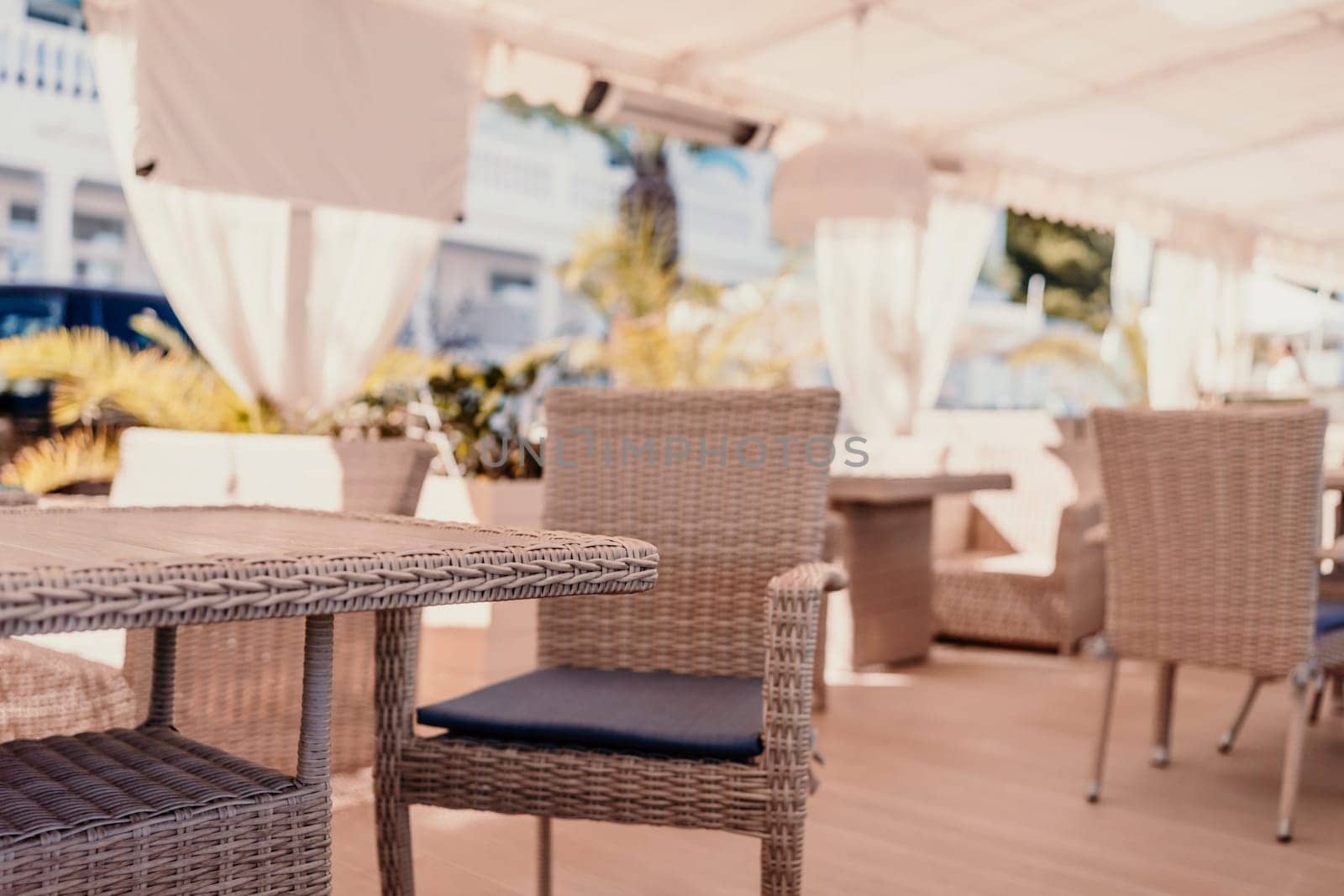 Wicker furniture tables in the open air are waiting for visitors. The interior of the restaurant in the open air. Empty tables of street cafe
