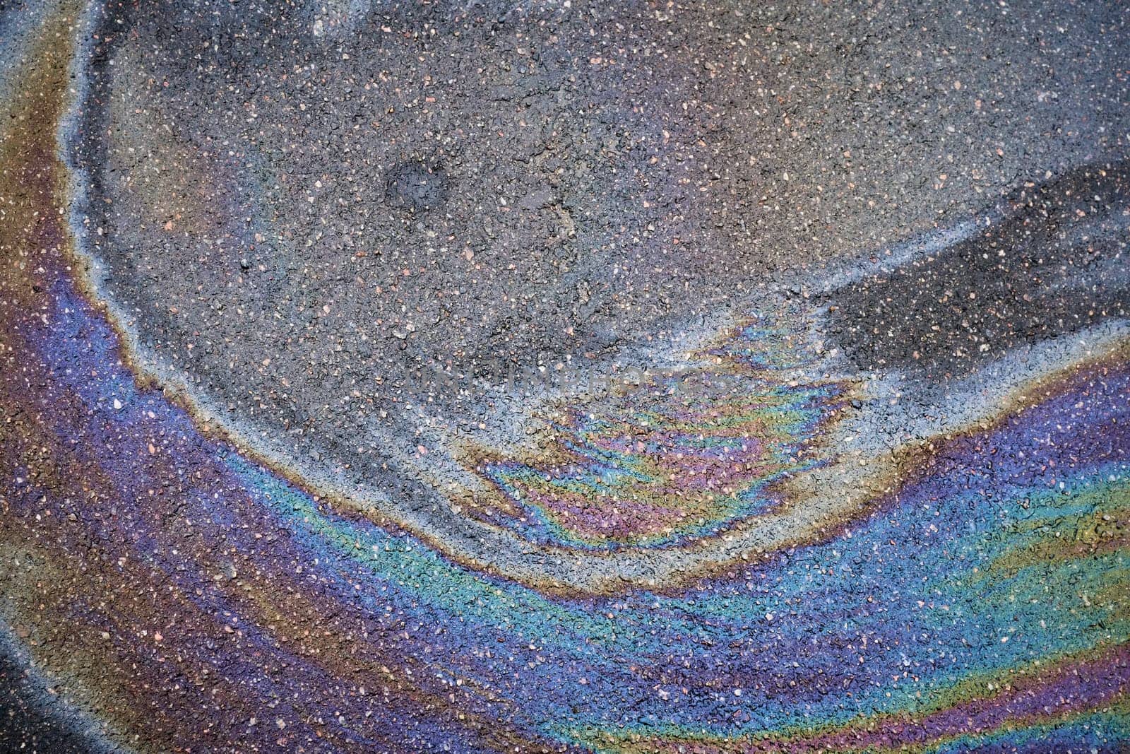 Rainbow gasoline spill creating colorful pollution on wet asphalt road