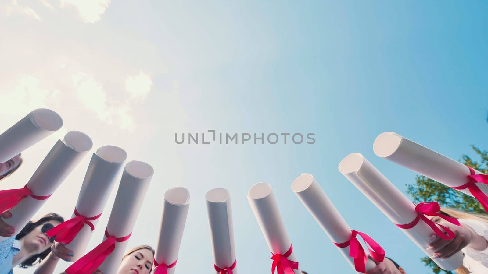 Graduates join their diplomas in a circle against the sky