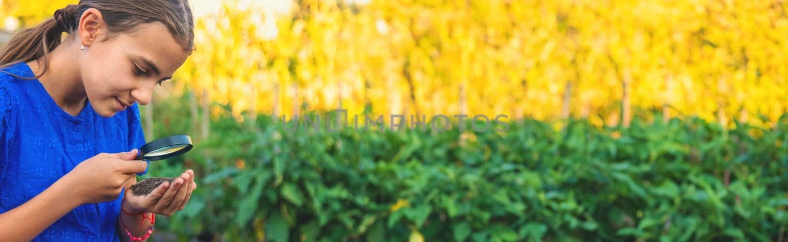 A child looks at the soil through a magnifying glass. Selective focus. Kid.