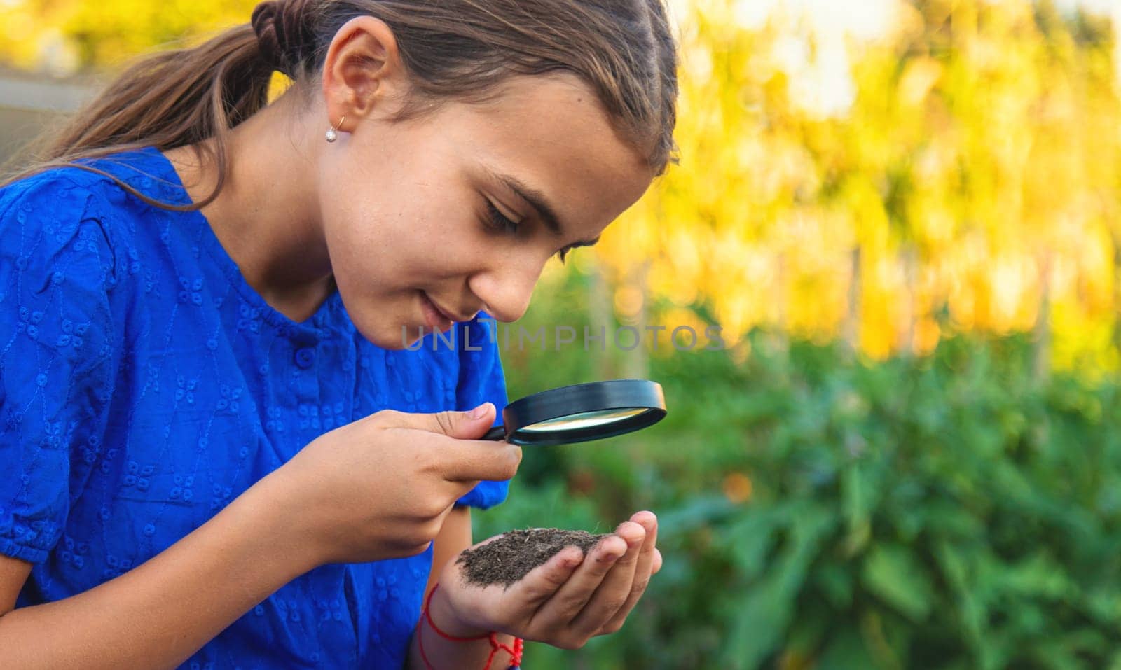A child looks at the soil through a magnifying glass. Selective focus. Kid.