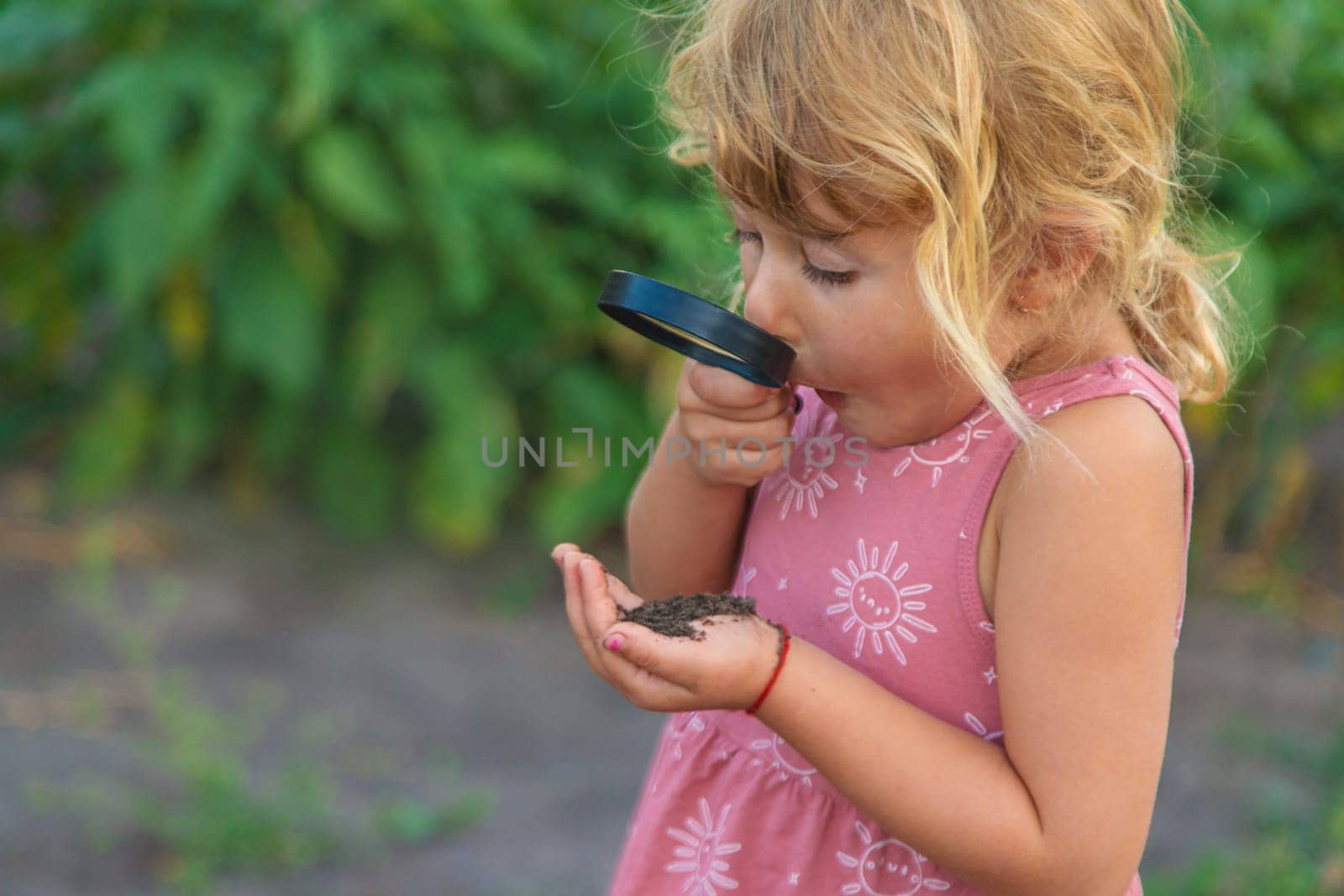A child looks at the soil through a magnifying glass. Selective focus. Kid.