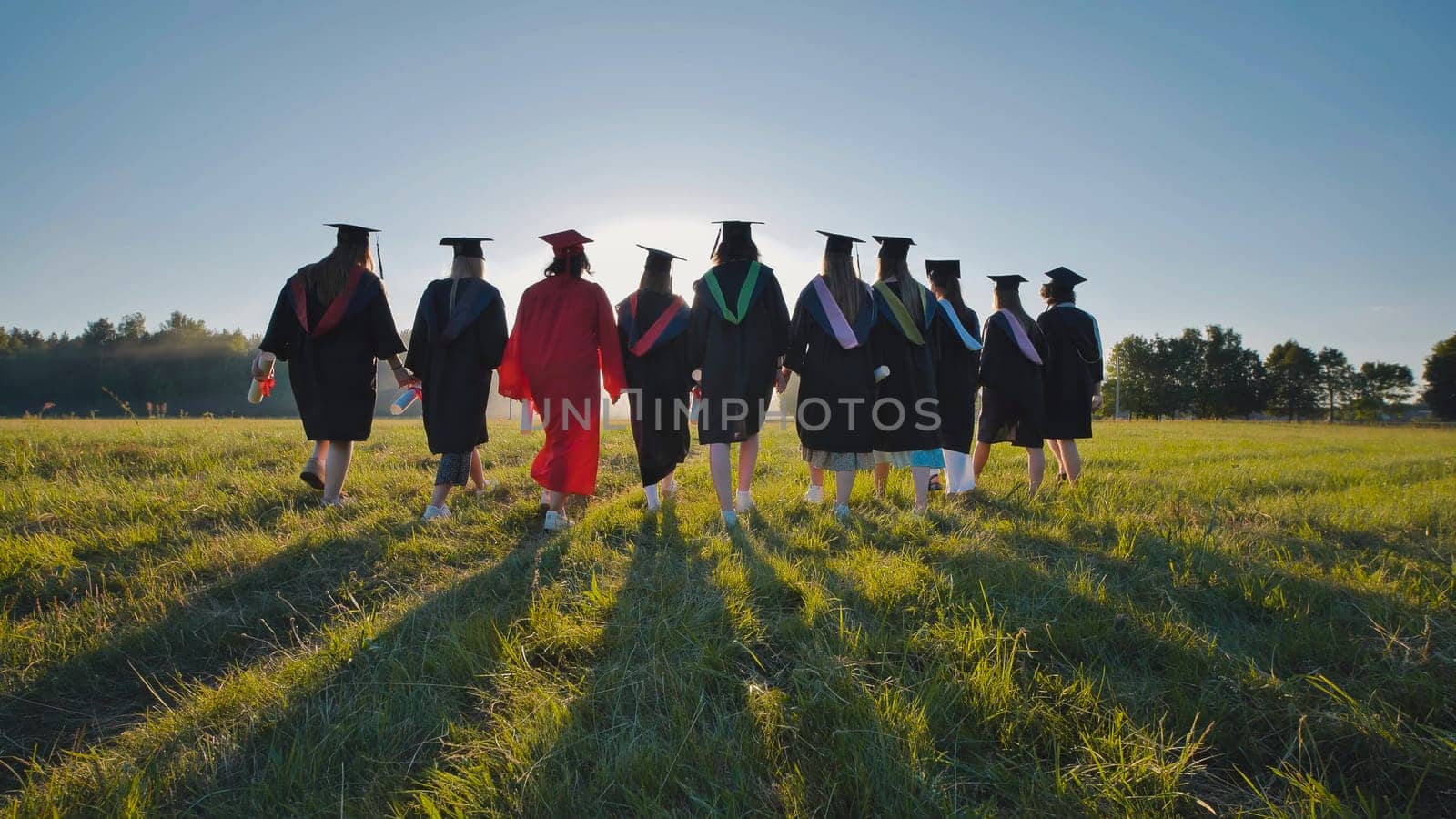 Six graduates in robes walk against the backdrop of the sunset.