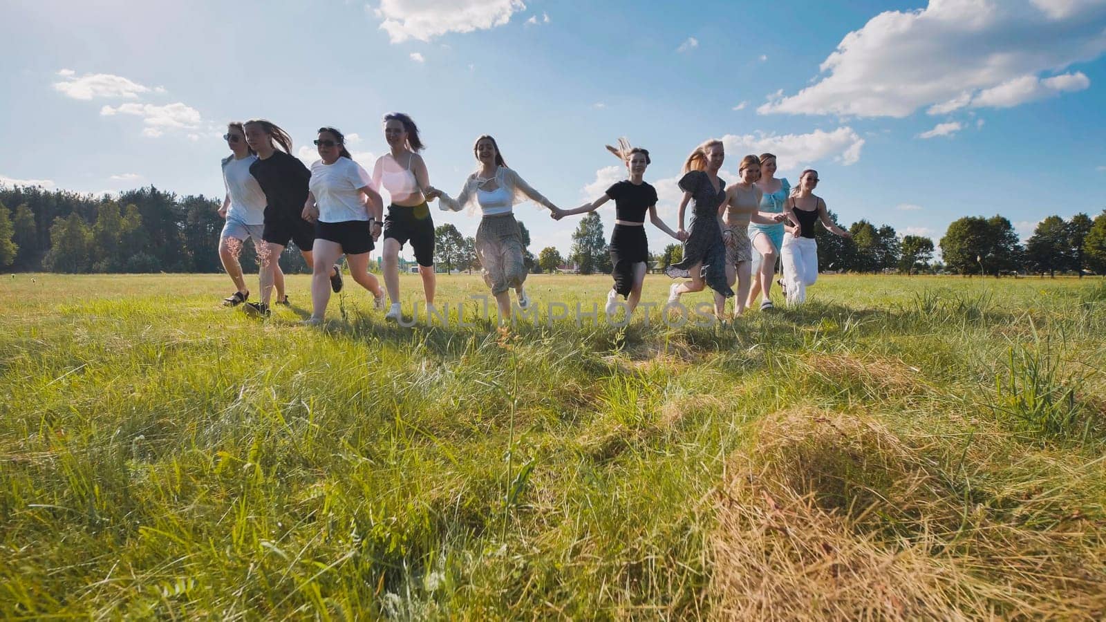 Group of friends is running through a field, holding hands and celebrating their graduation