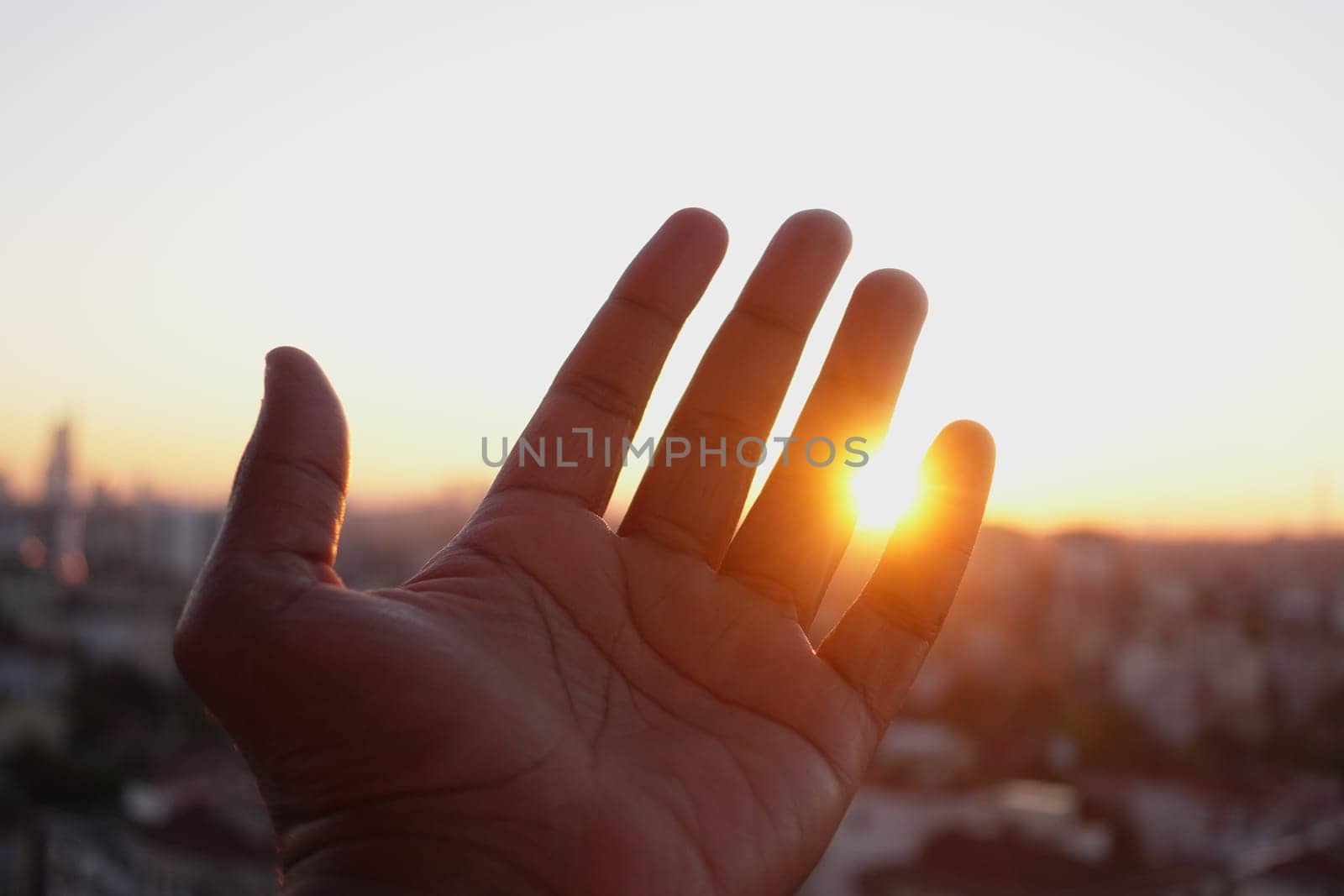 A hand is gently reaching out towards the warm sunlight in front of a stunning city skyline
