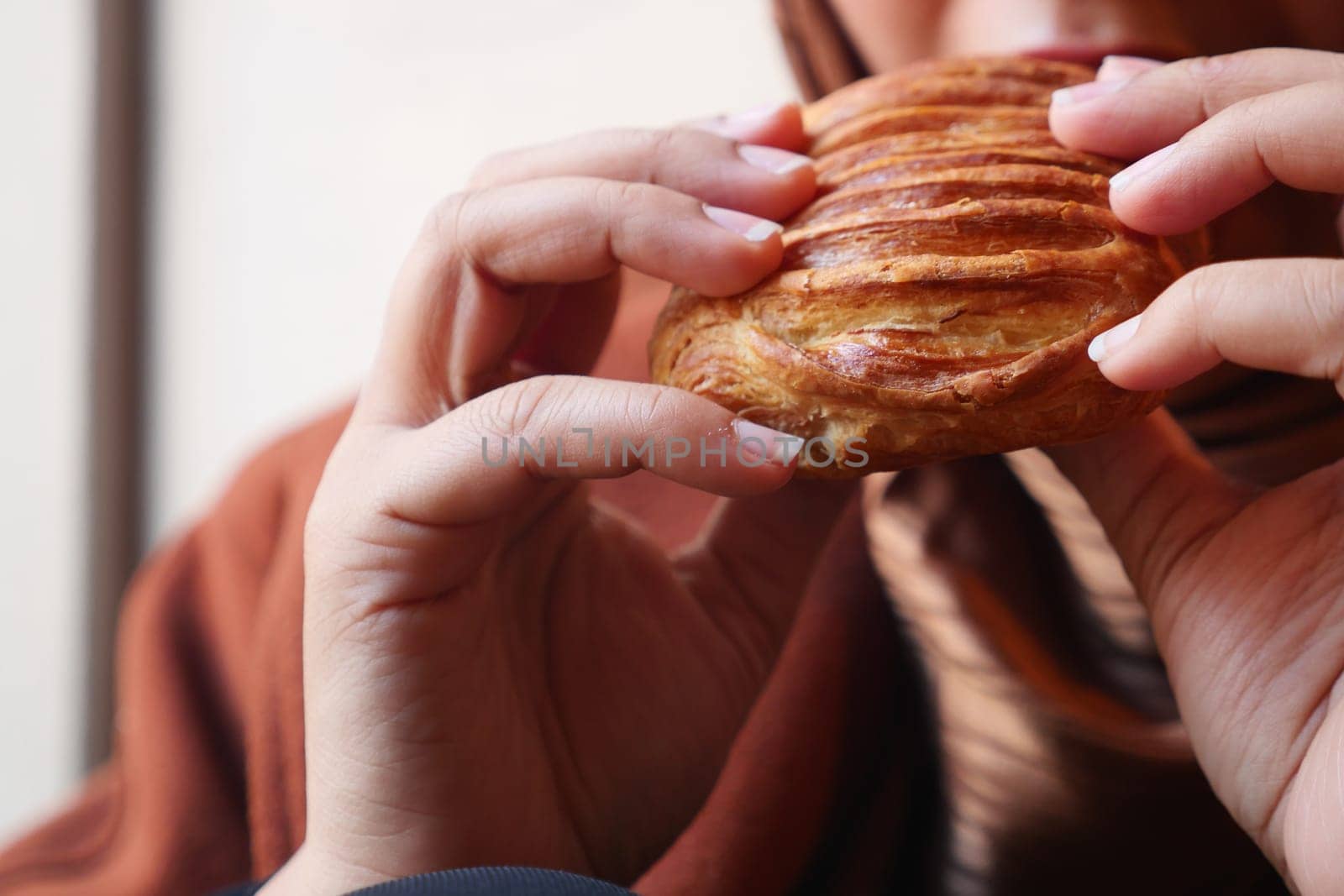 A person holds a golden pastry, ready to bite in a warm atmosphere of fresh baked goods