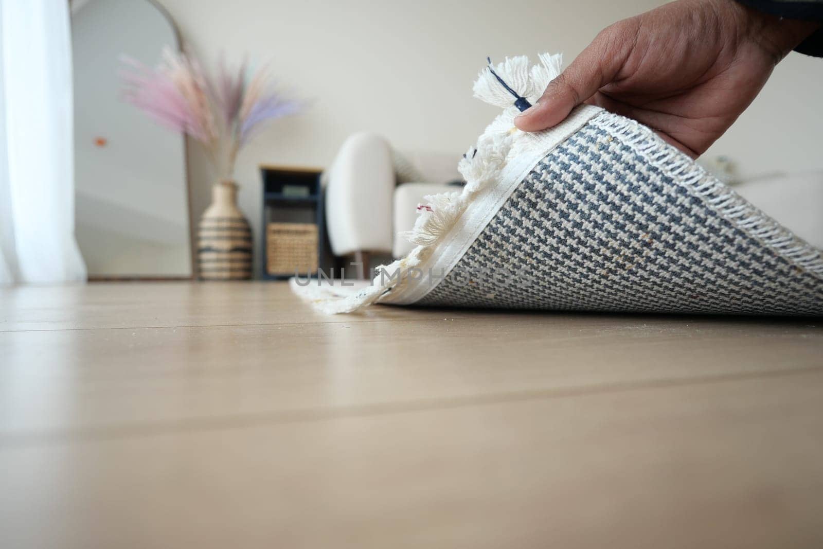 A hand carefully rolls up a beautifully patterned rug in an elegant and stylish interior setting
